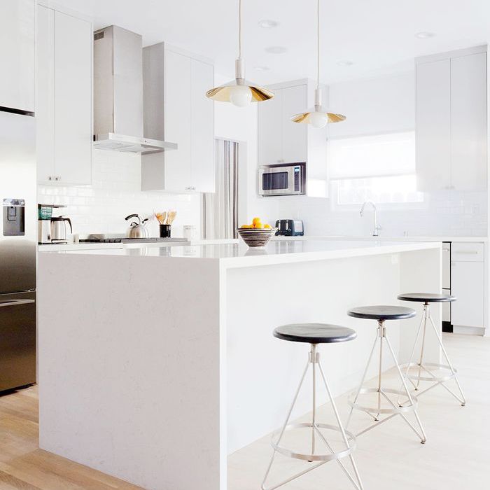 光滑的白色厨房与三个圆形酒吧凳子和吊灯