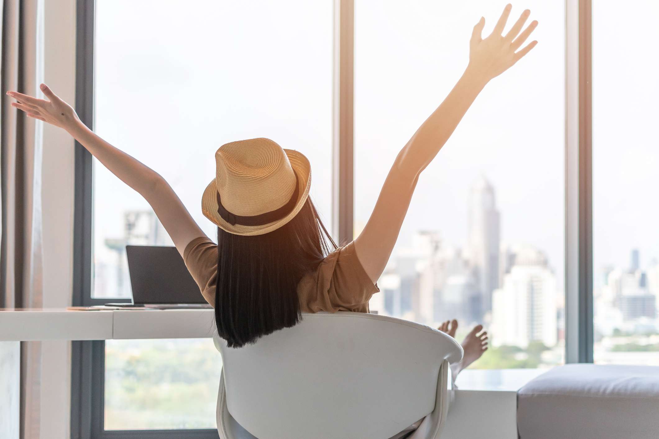 女子拥有她的双手举过头顶兴奋而来自酒店房间的椅子城市风景拍摄。