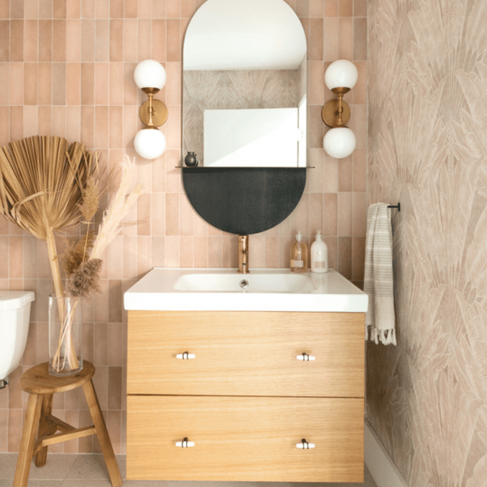 化妆室里有一面椭圆形镜子，两个球形灯罩，两种桃色墙纸