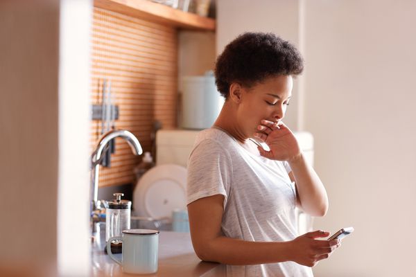 打呵欠在她的厨房的困妇女在一杯咖啡旁边。