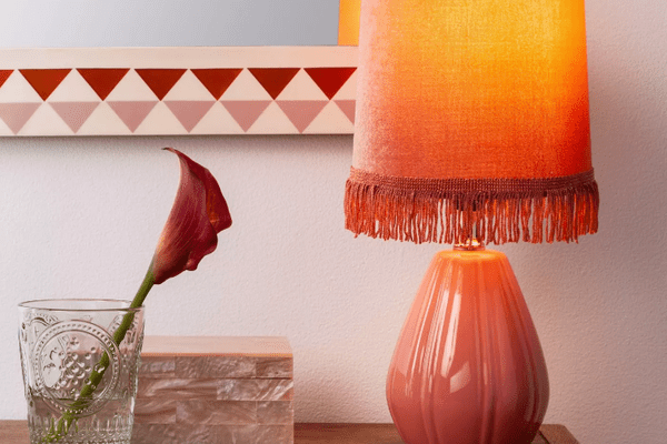 在一个装饰性的盒子前面，有一盏放在控制台上的粉色台灯，玻璃花瓶里插着一株粉红色的兰花。