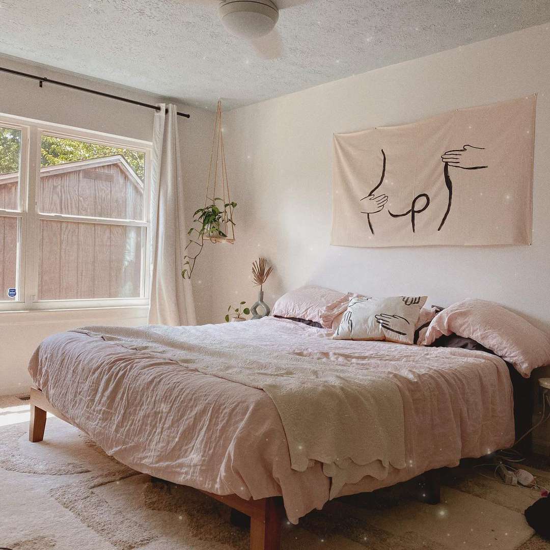 中性卧室，粉红色的床上用品和悬挂植物。