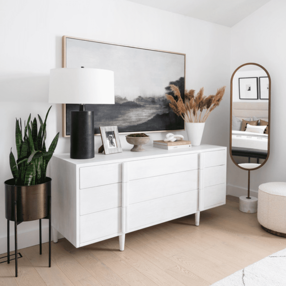 一张白色的控制台桌子，上面装饰着一盏时髦的灯，一株蛇草和一个盛满潘帕斯草的花瓶