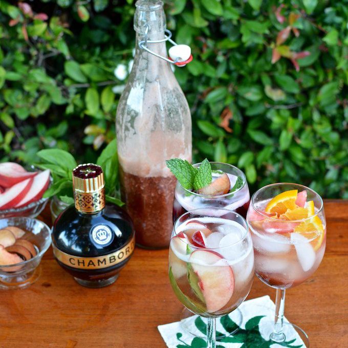 两杯桑格利亚汽酒和一瓶香槟酒放在木桌上;背景是绿色植物。