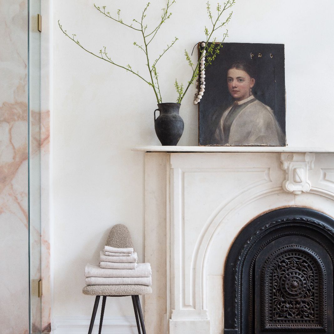 一间白色的房间，有一座壁炉，一张放满毛巾的凳子和一个大理石壁炉架。