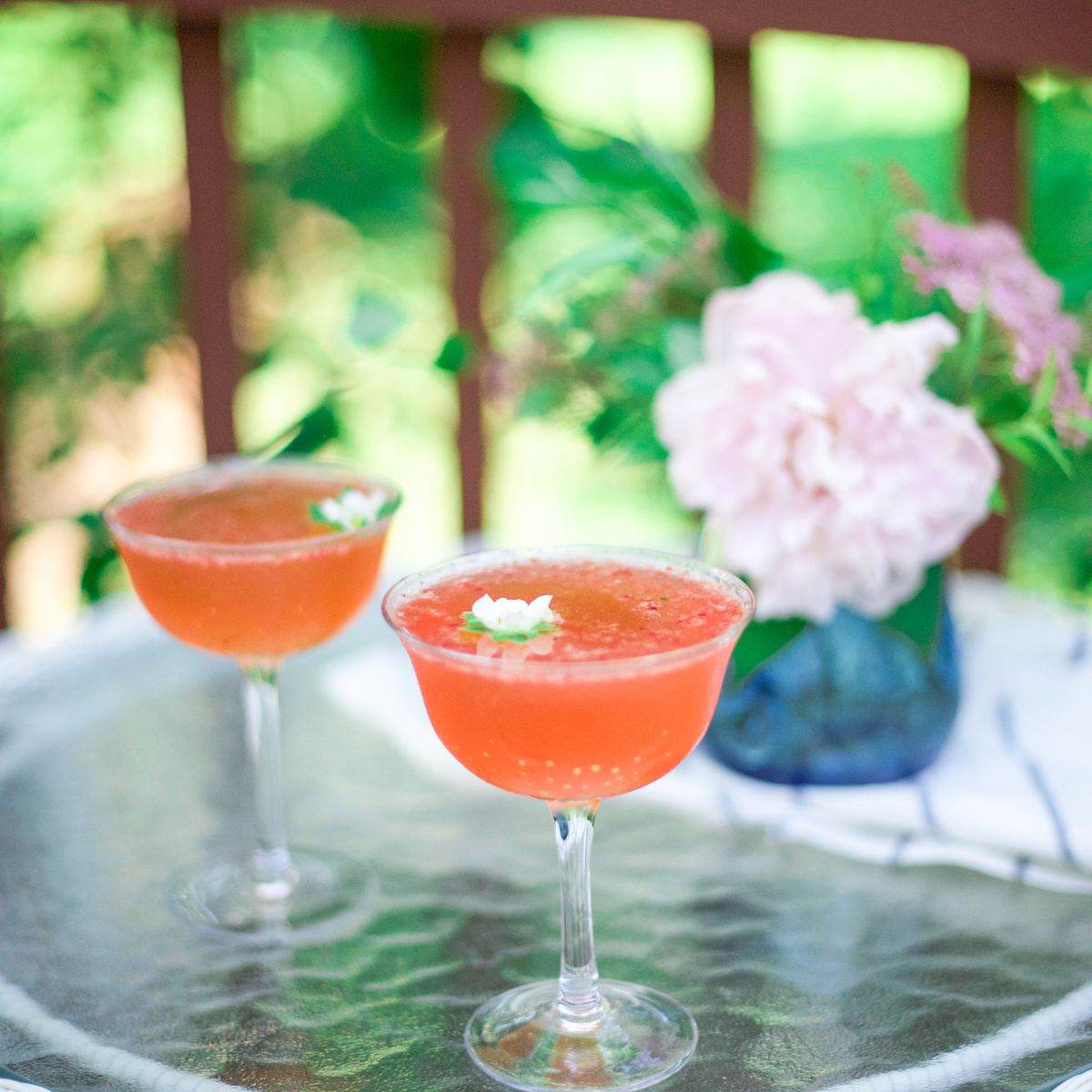 Strawberry cocktail in a coupe glass with flower garnish.“class=
