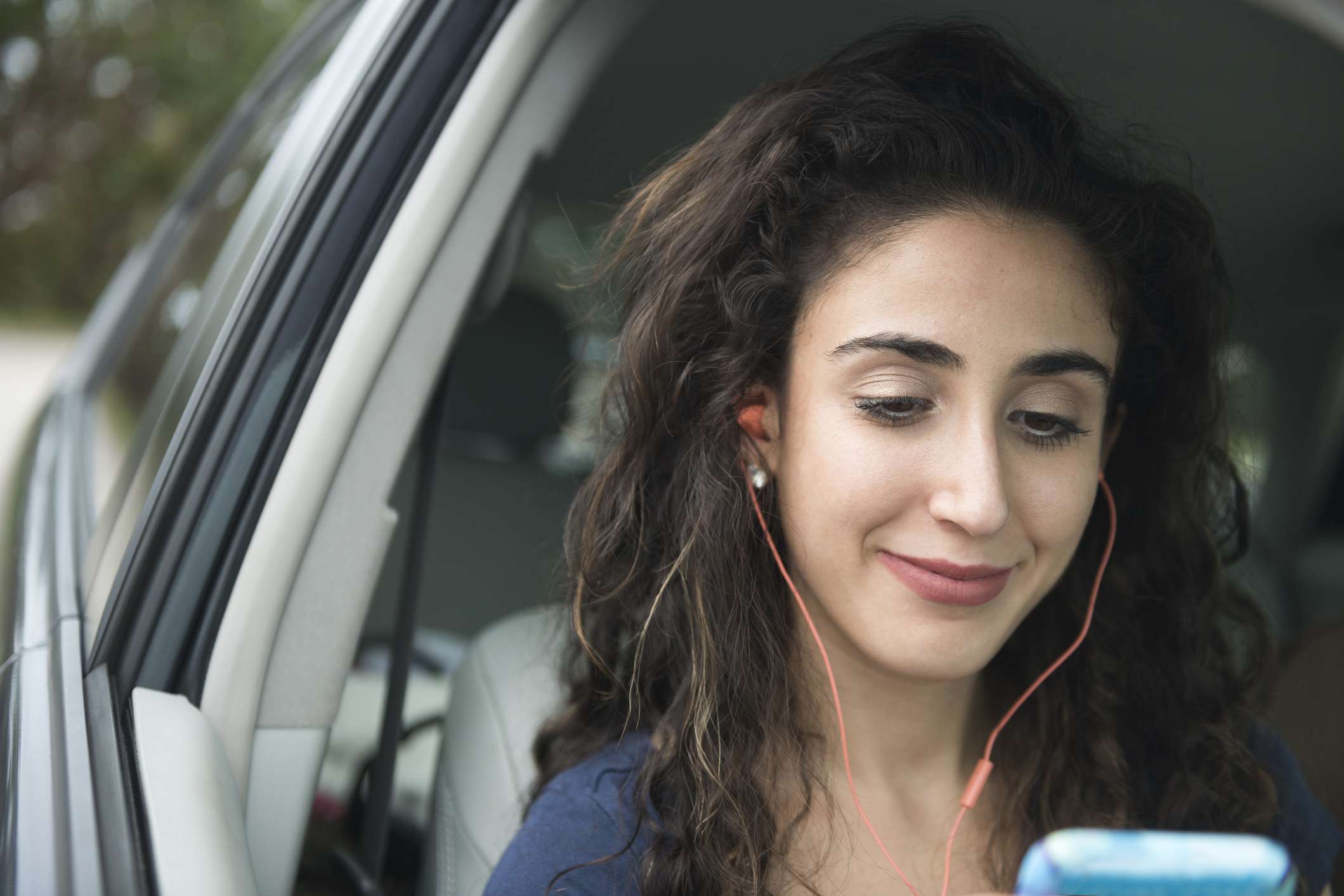 一名女子在车里一边听着耳机，一边看着手机。