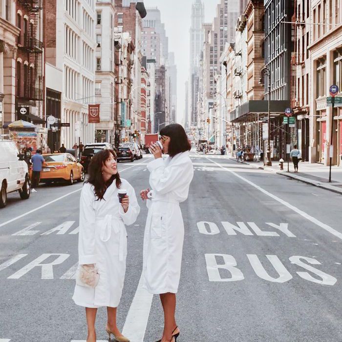 两个女人抱咖啡杯，站在城市街道的中间。