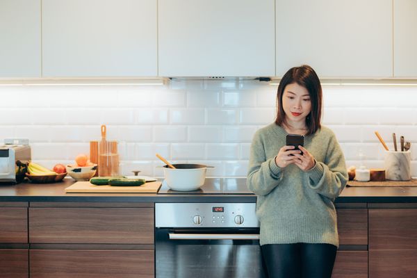 年轻女子倾斜厨房柜台，使用智能手机