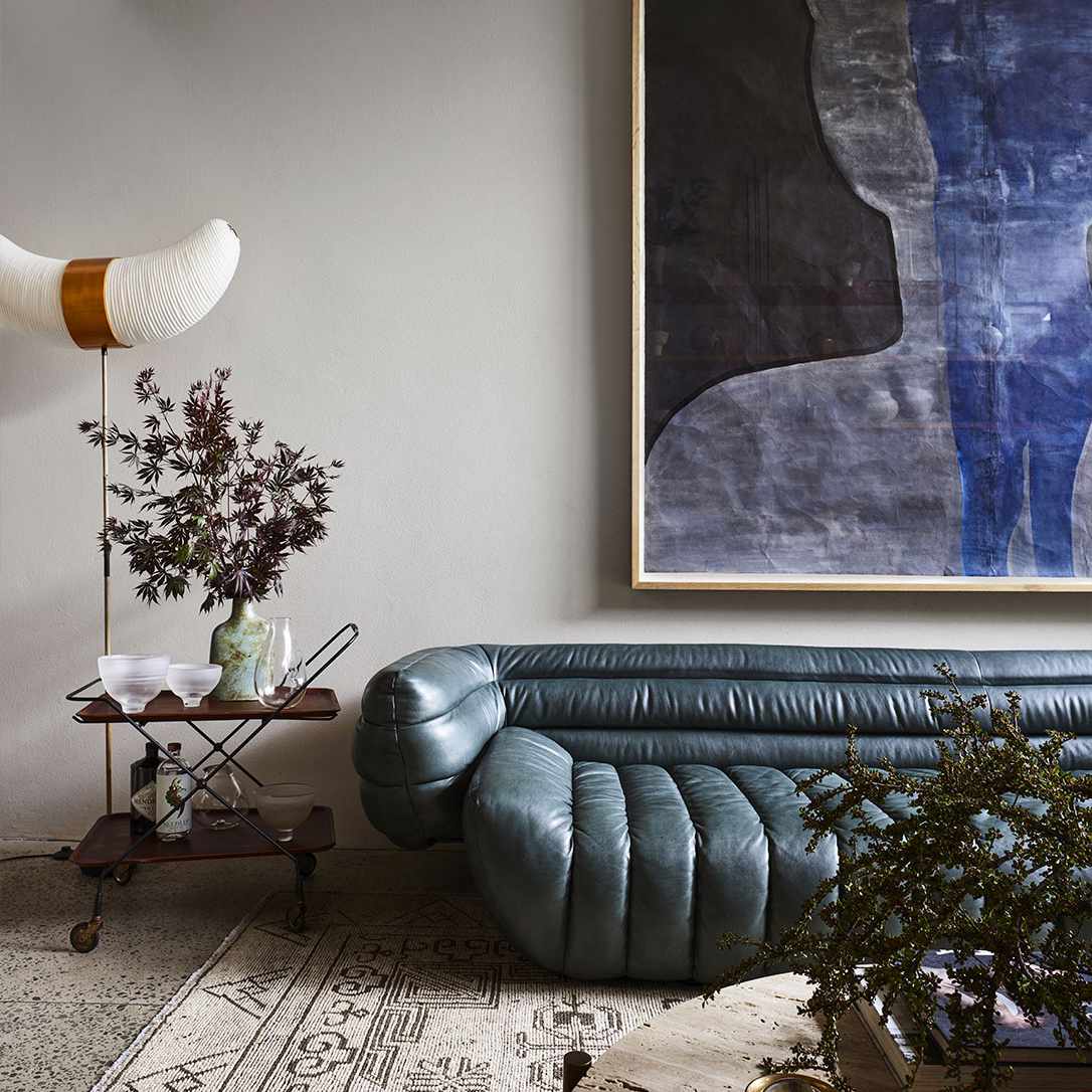 一个世纪五六十年代的客厅，温馨，牛仔蓝，通道簇绒真皮沙发和墙壁上的大的蓝色抽象绘画。