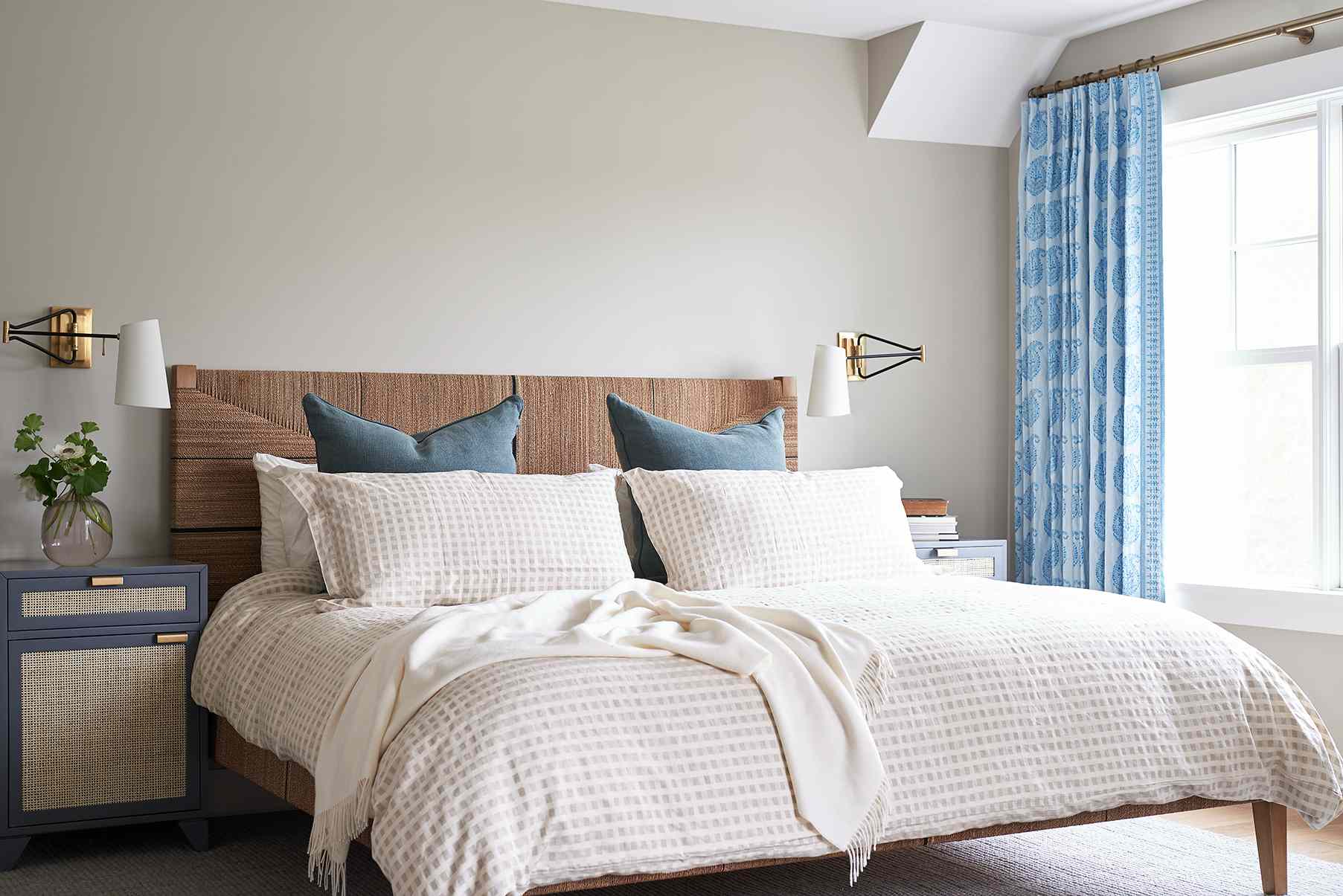 一间现代沿海卧室，装饰着白色格子毯，蓝色枕头和蓝色佩斯利窗帘