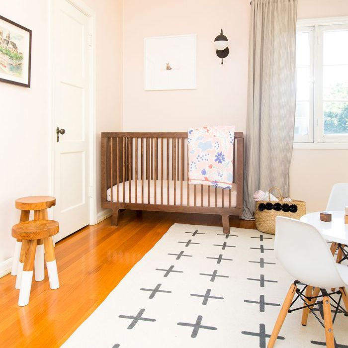 淡粉色的墙壁和深色实木婴儿床“class=