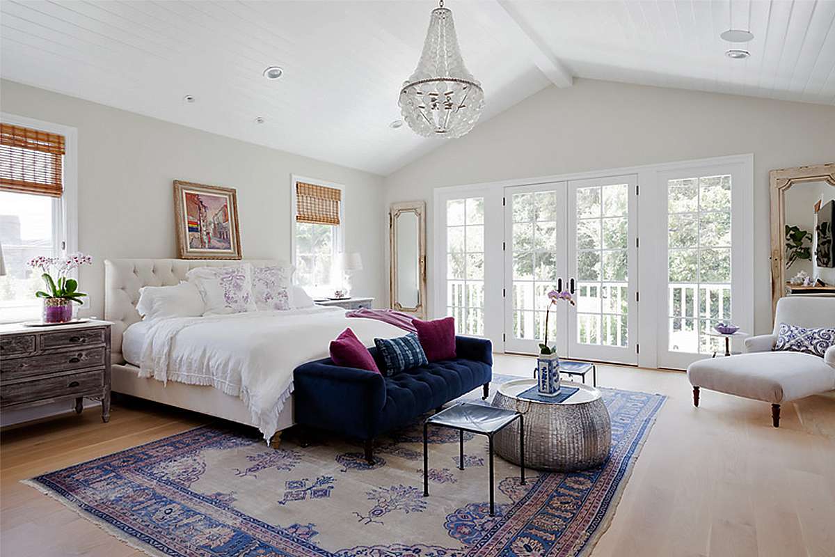 一间通风的全白色卧室，有一盏吊灯和海军蓝绒簇绒沙发。