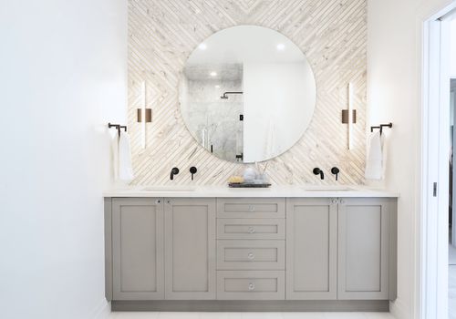 A bathroom with gray cabinets and a white tile-lined wall