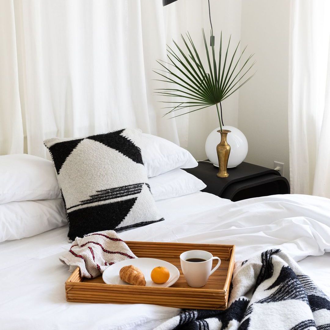 舒适的白色床，早餐托盘和棕榈叶。