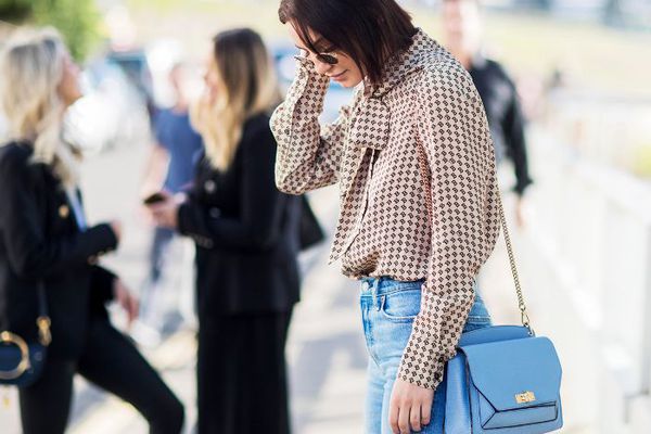 一个女人穿着一个长链的蓝色斜挎包。