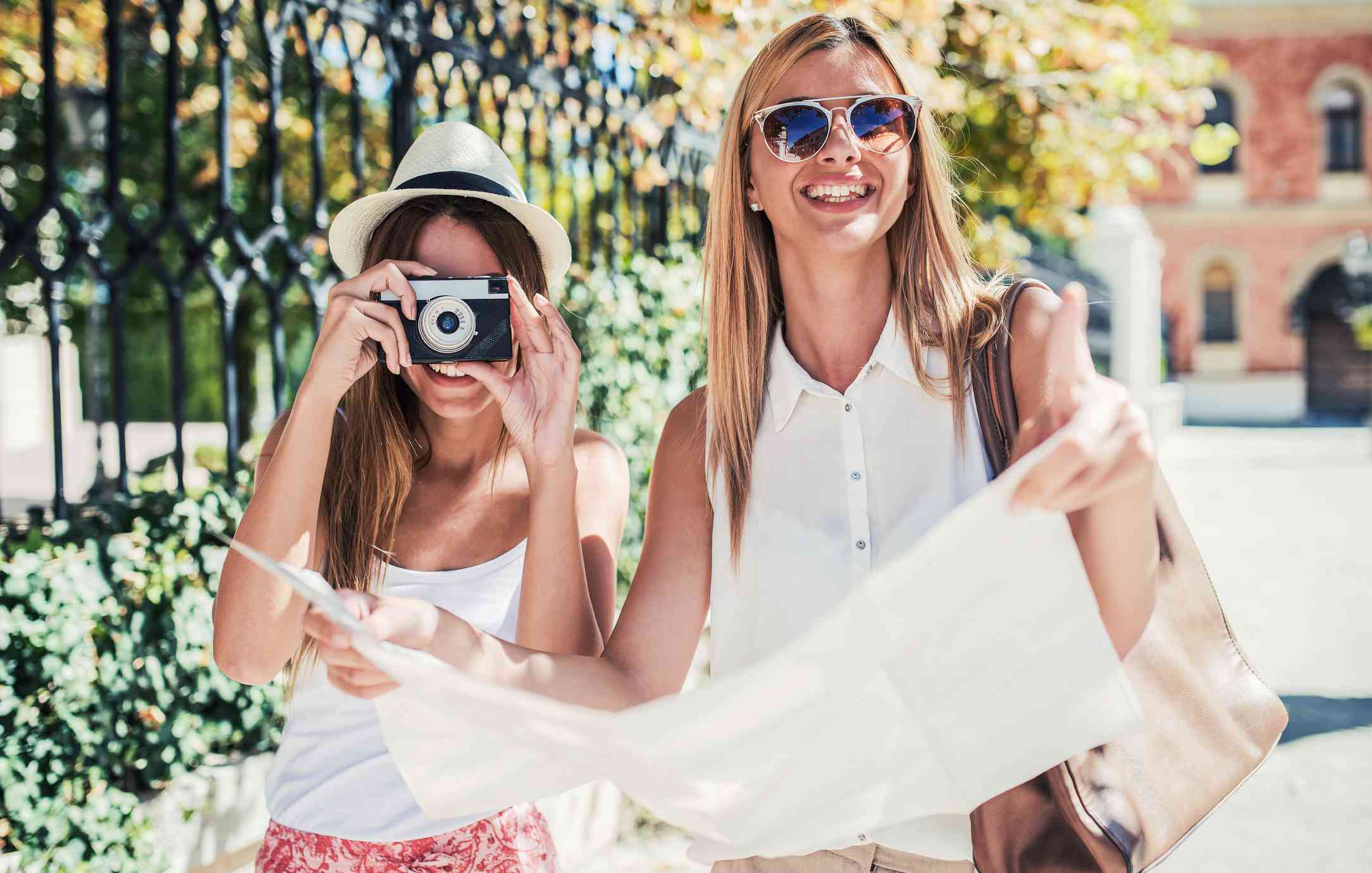 两个女人拿着纸地图和相机摆姿势。