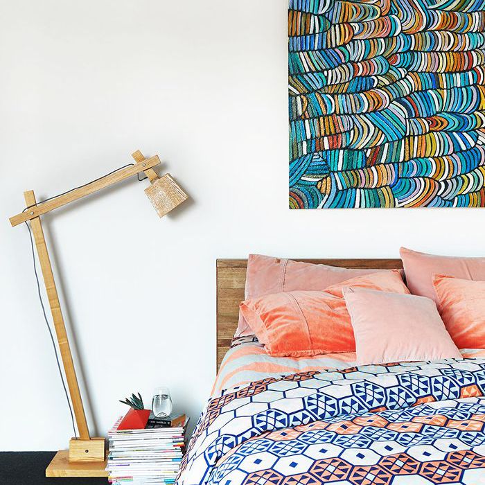 一个低矮的床，配有几何印花羽绒被和粉红色天鹅绒枕头。