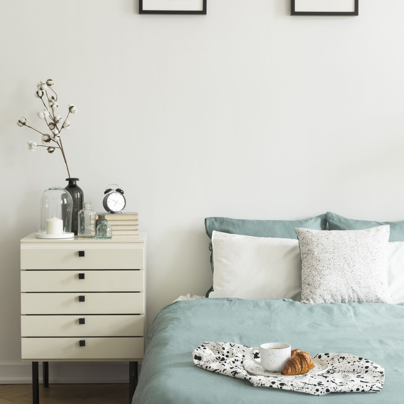 白色的卧室内用早餐放在床上，枕头和柔和的绿色床上用品，两个简单的海报和床头柜与装饰实景照片