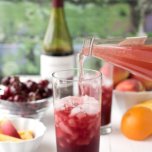 在柯林斯酒杯里的红酒鸡尾酒，周围环绕着新鲜的水果。