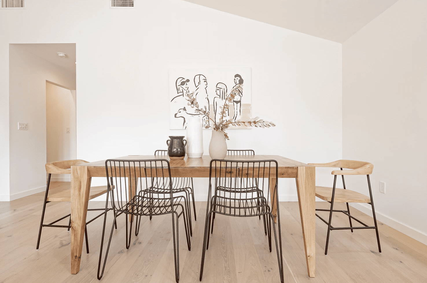 一张木制餐桌，上面装饰着一个黑花瓶、一个白花瓶和一个米色花瓶