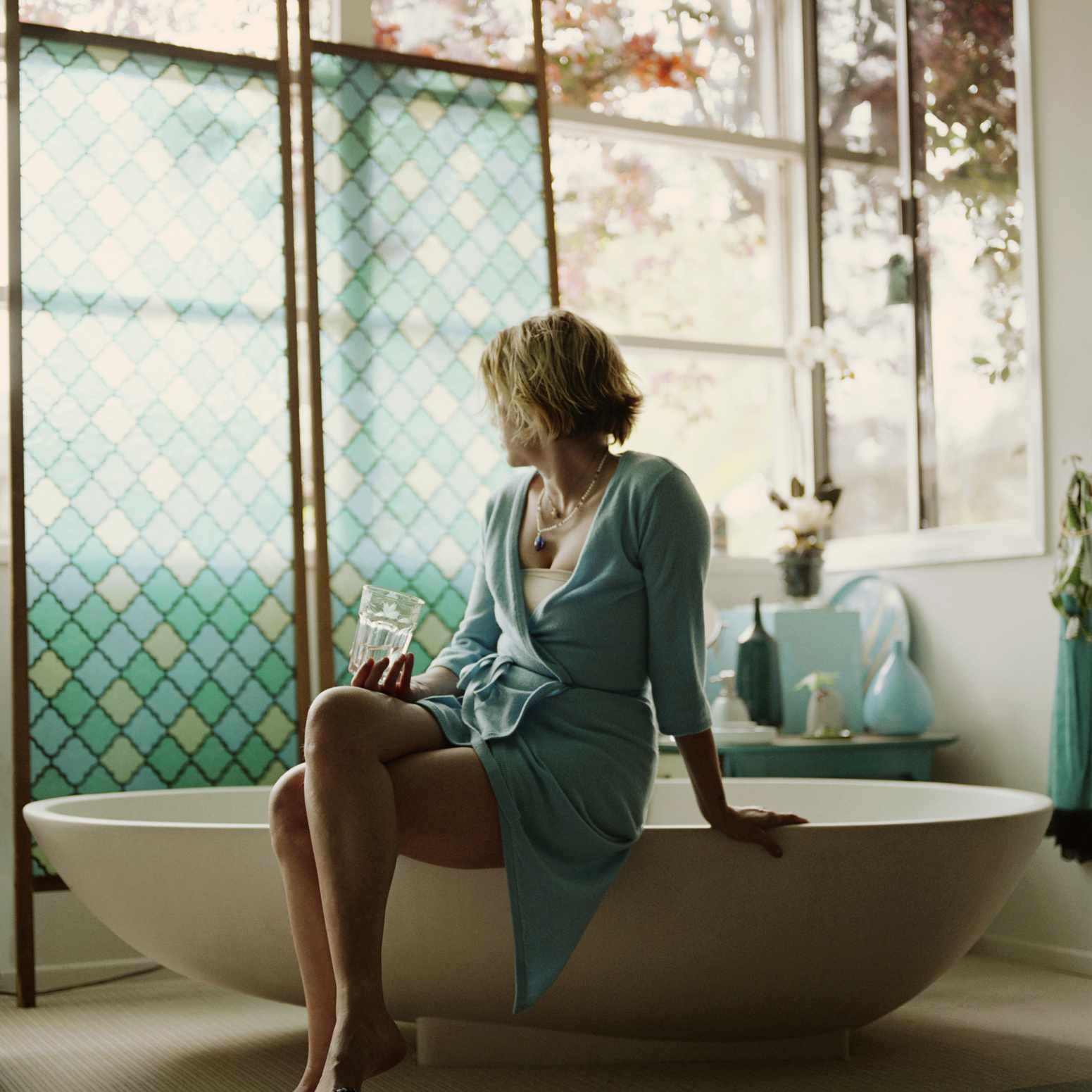 一个女人在浴缸边放松，同时看着窗外。