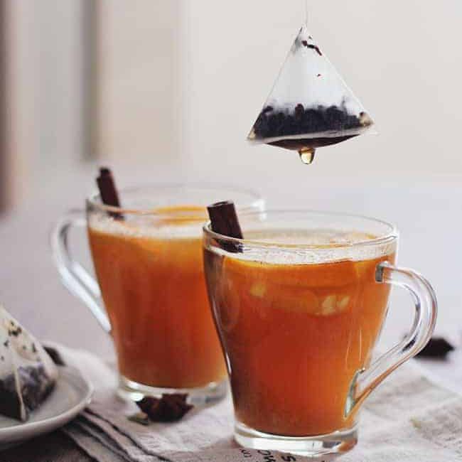 茶鸡尾酒在两个玻璃杯，装饰着肉桂棒。”class=