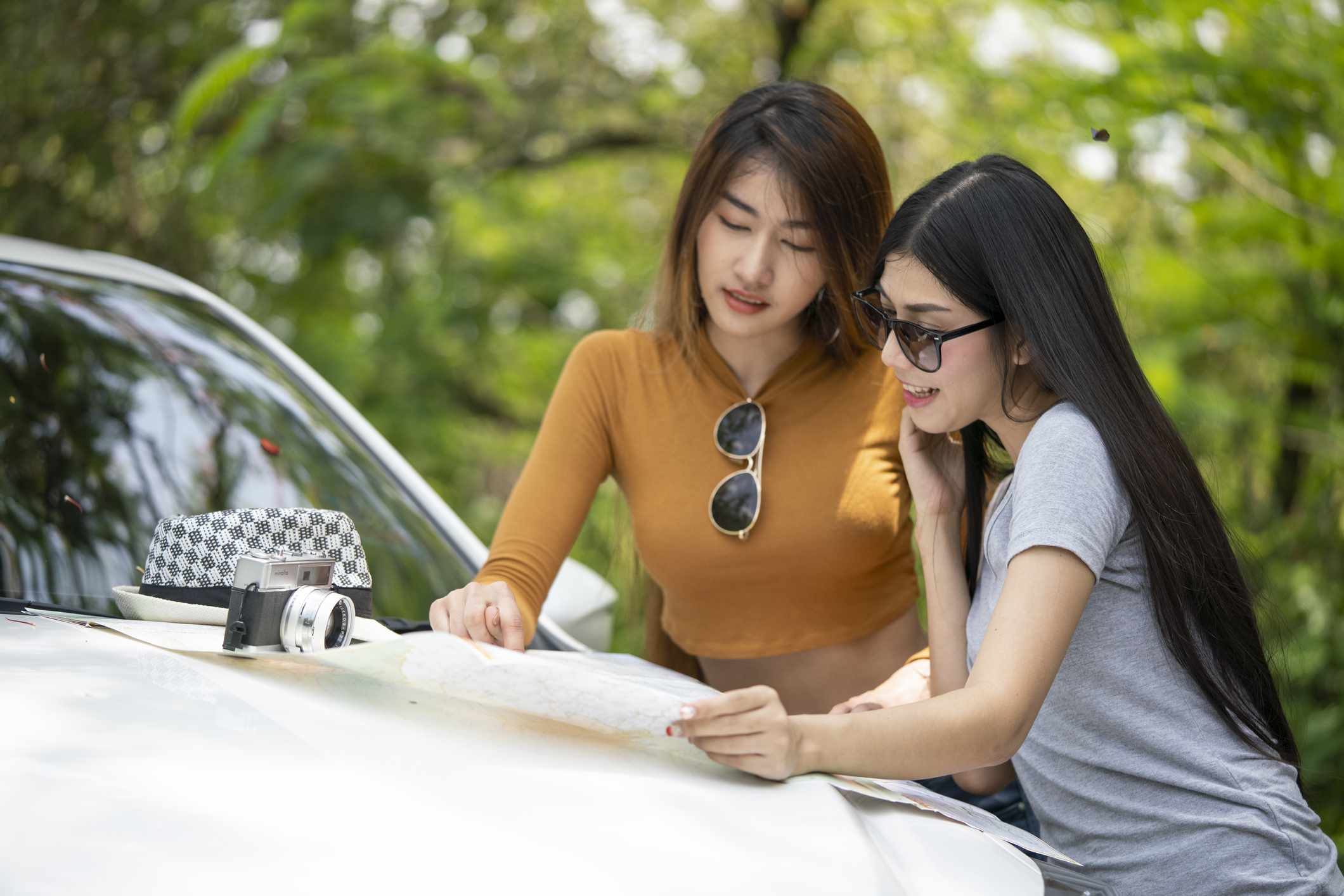 两名妇女检查放置在汽车的引擎盖纸质地图。