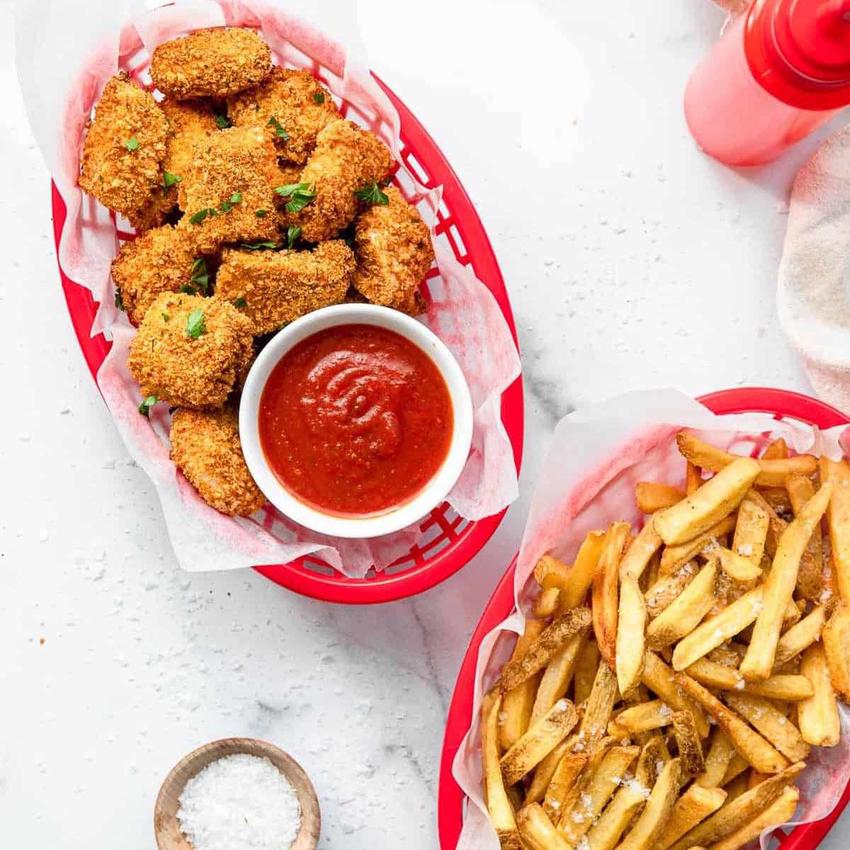 一盘鸡块放在一盘薯条旁边