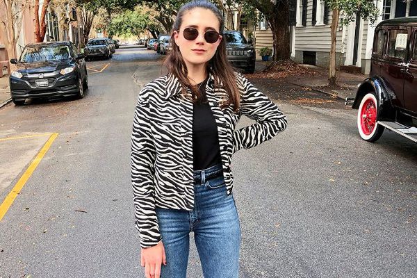 一个棕色头发的女孩戴着墨镜，穿着斑马图案的夹克，黑色t恤和牛仔裤。