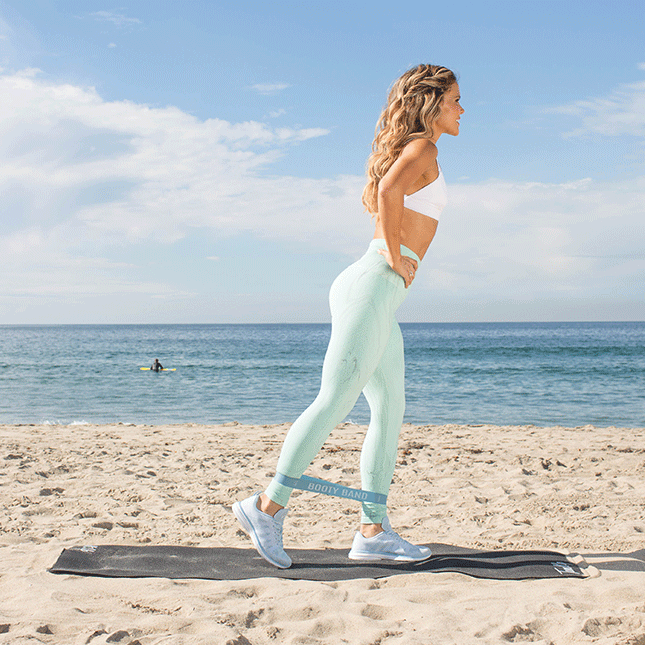 一个女人在海滩上做Booty Band的回扣练习