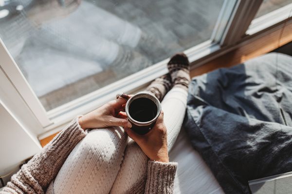 拿着咖啡的女人站在窗边