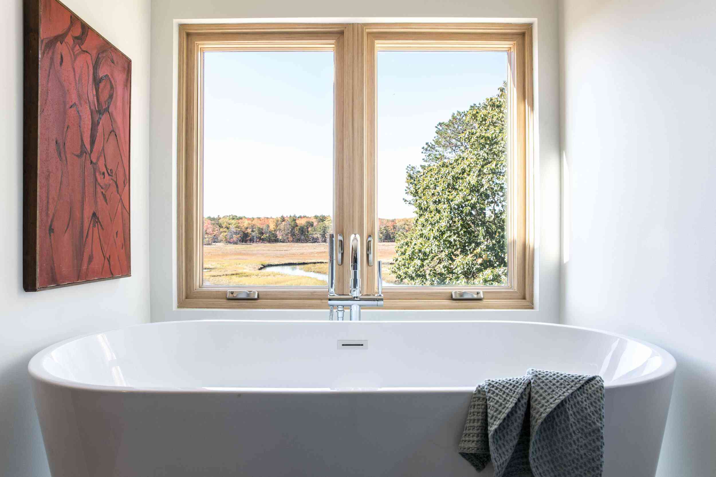 白色的浴室里有一个锡灰色的浴缸和一幅红色的画