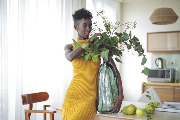 一个年轻的黑人女人，穿着黄色的衣服，拿着一个大花瓶，里面有一株植物。