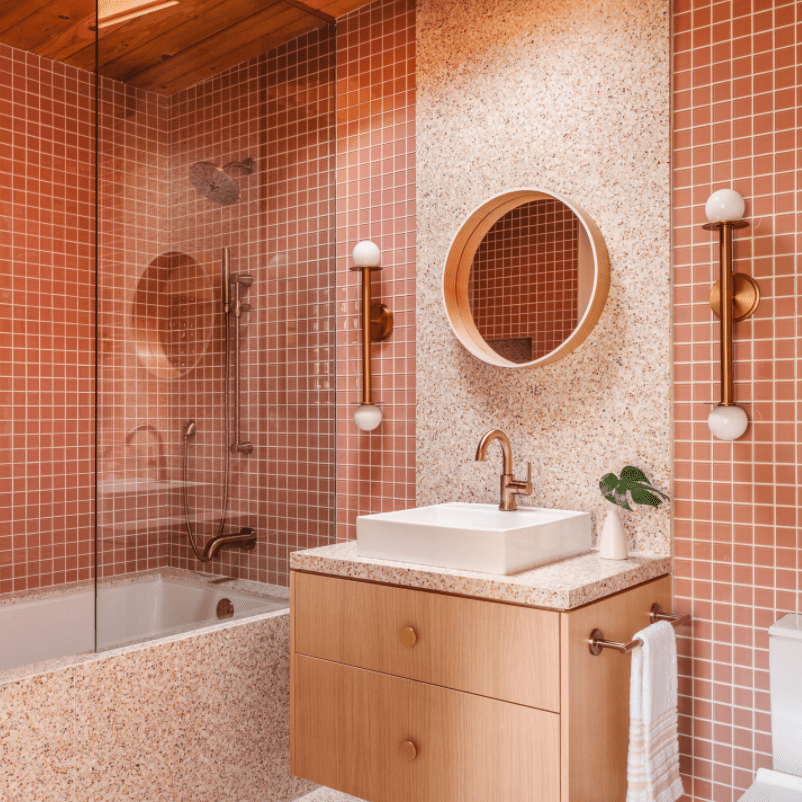 粉红色的浴室充满了几何元素:圆形镜子、矩形水槽、方形后挡板砖等等