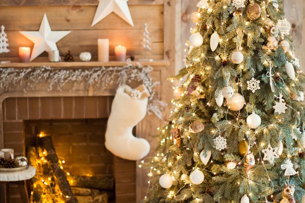 壁炉前装饰有白色和金色装饰物的圣诞树，圣诞树上有长统袜和礼物