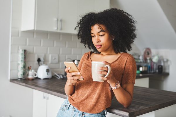 年轻女子一边打电话一边在厨房喝咖啡
