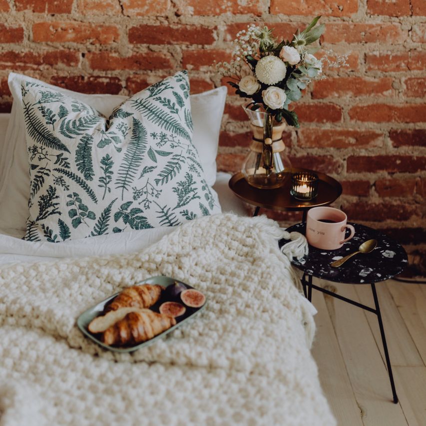 卧室有裸露的砖墙，在床旁边的圆形床头柜上放着一瓶花