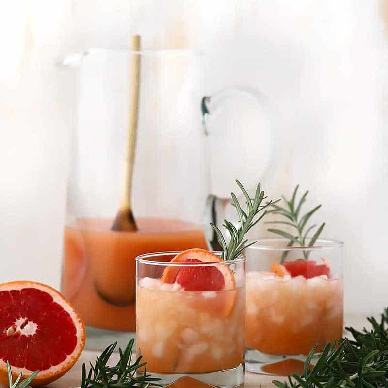 Grapefruit cocktail in a glass with crushed ice and a rosemary sprig.“class=