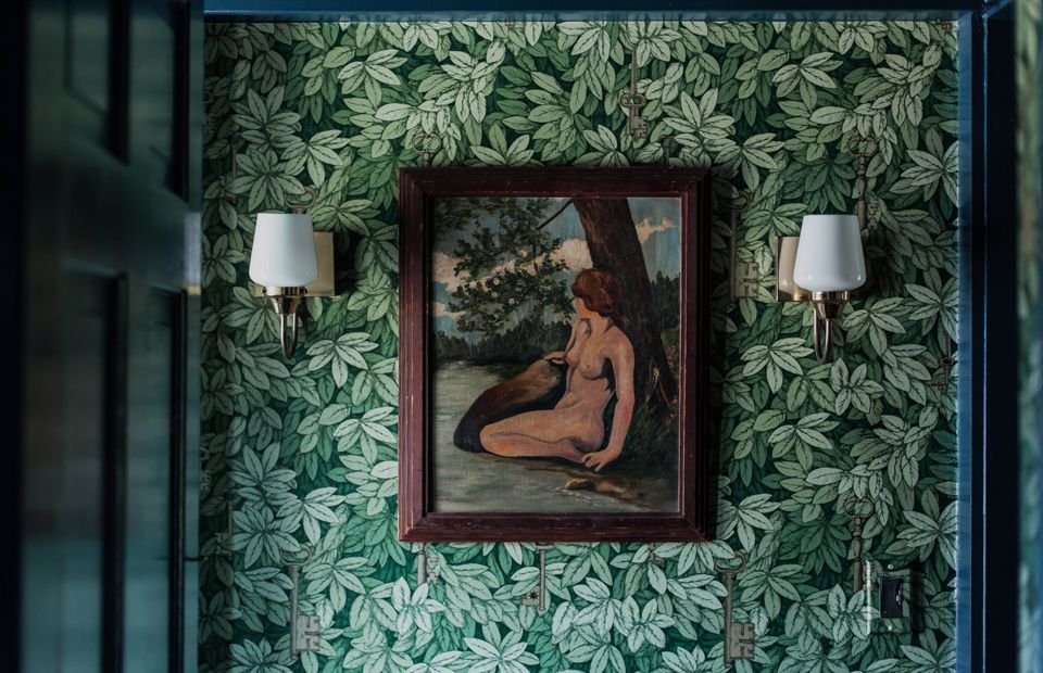 A hall covered in green leaf wallpaper with a painting on top