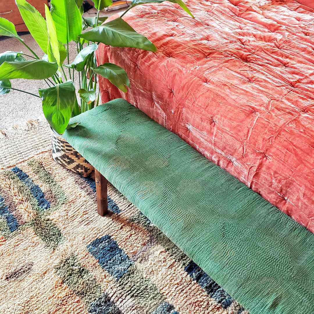 一只天堂鸟坐在床脚下的绿色软骨长凳旁边。