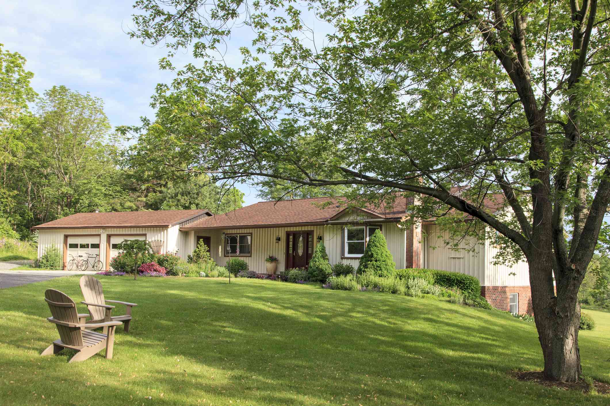 牧场风格的房子与郁郁葱葱的绿色草坪有两把阿迪朗达克椅子和树