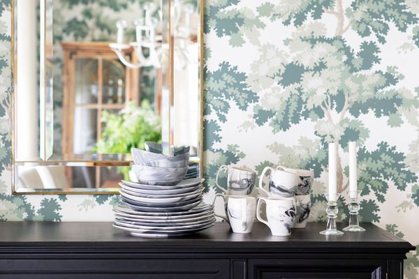 Antique side table with porcelain china and printed wallpaper behind it.
