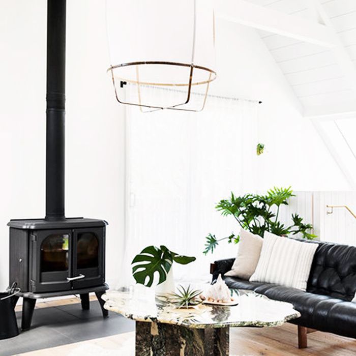 一个白色的极简主义的生活区，有一块弗洛卡蒂地毯，一个黑色的木火炉，一张黑色的皮沙发，