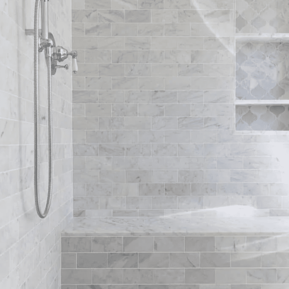 A shower lined with light gray tiles