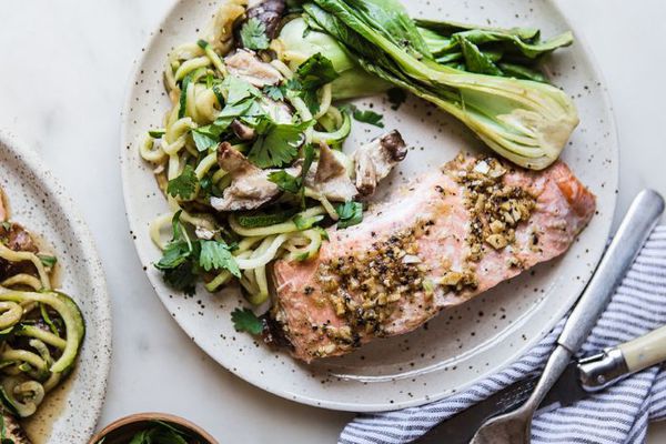 一盘三文鱼，Bok Choy和夏南瓜面条用餐巾，刀子和叉子。