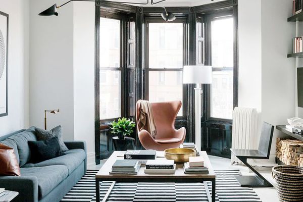 白色围墙的客厅，配有蓝色的沙发，黑色的大吊灯现代，粉红色的蛋椅，黑色和白色条纹的地毯。