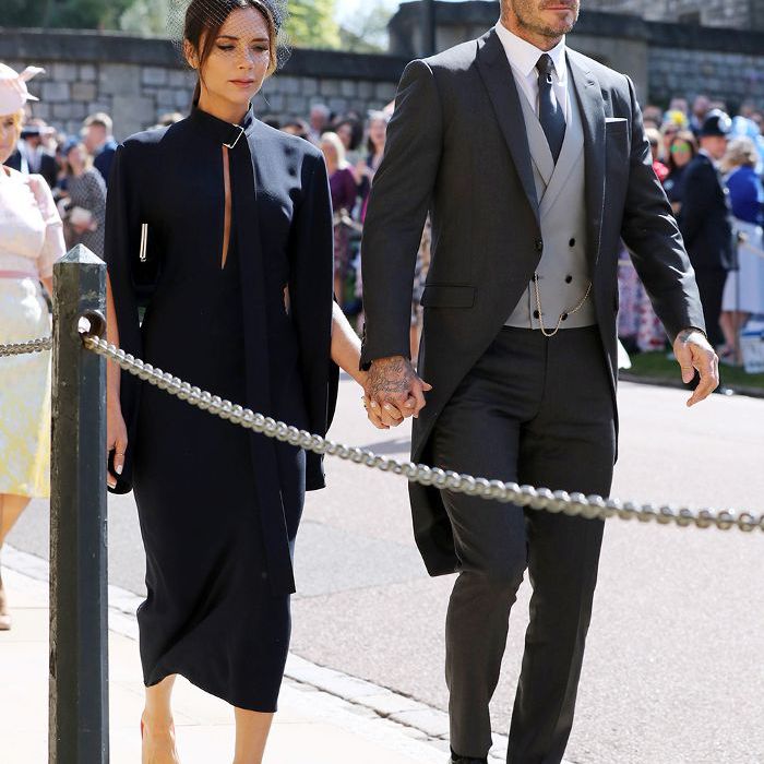 梅根和哈里的皇室婚礼嘉宾的行头:维多利亚·贝克汉姆身穿海军蓝中长裙，脚上穿着红色鞋子，旁边站着大卫·贝克汉姆